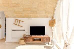 A modern living room with a stone wall, a flat-screen TV, a wooden cabinet, and a woven basket. - Lovely Villa w/ Pool & Garden, close to beaches (Pescoluse)