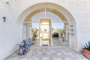 A building entrance with an arched doorway, a large glass window, and a stone sculpture on the ground. - Lovely Villa w/ Pool & Garden, close to beaches (Pescoluse)