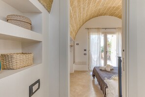 Une chambre d’hôtel avec un lit, une étagère avec des paniers, une porte donnant sur un balcon et un sol carrelé.