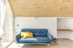 A room with a blue sofa, a yellow pillow, a metal magazine rack, and a window with curtains. - Lovely Villa w/ Pool & Garden, close to beaches (Pescoluse)