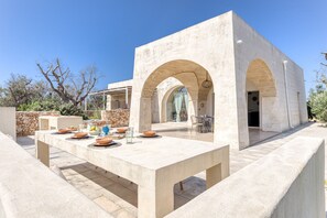 Un área de comedor al aire libre con una mesa y sillas de piedra, rodeada por un muro de piedra y vegetación.
