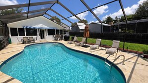 En swimmingpool med liggestole og parasoller, omgivet af en overdækket terrasse.