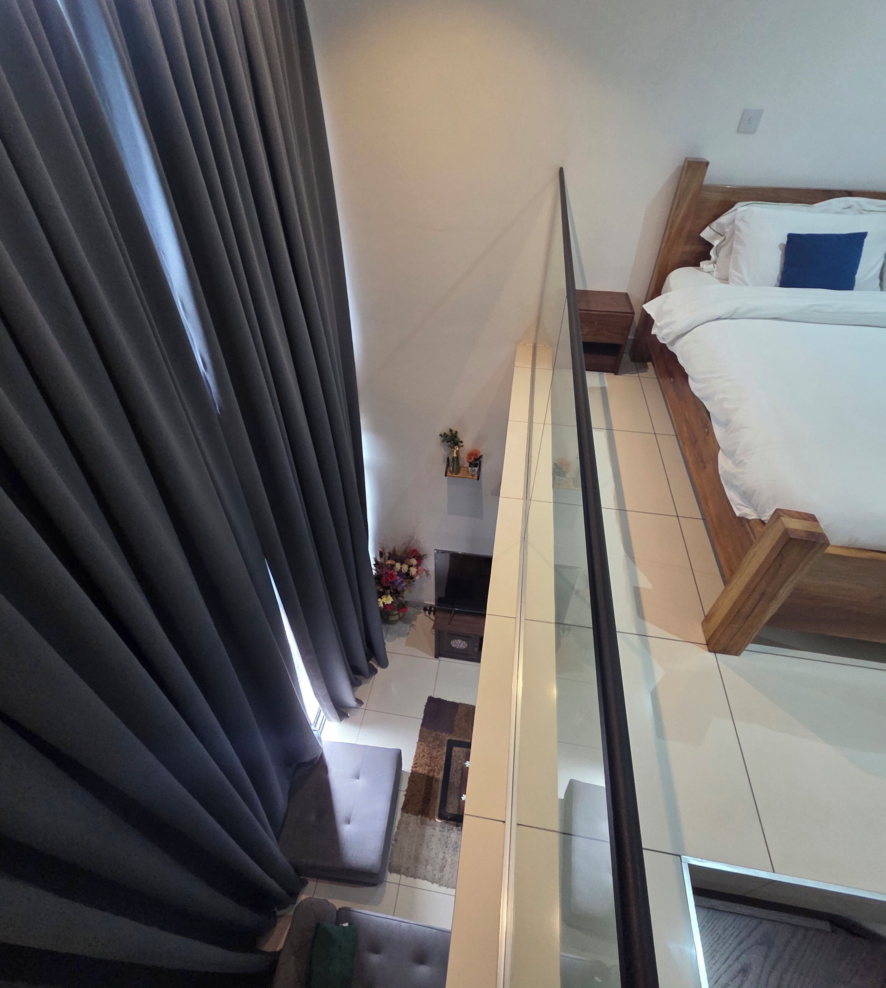 Ein Hotelzimmer mit einem Bett, einem kleinen Tisch mit Blumen und Blick durch Vorhänge nach draußen.