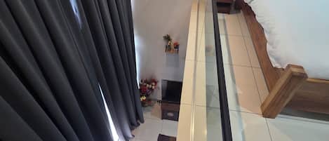 A hotel room with a bed, a small table with flowers, and a view of the outside through curtains.