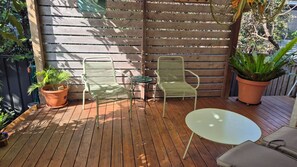 A wooden deck with two metal chairs and a small table, surrounded by potted plants. - Beachwood Villa - Modern Townhouse Walk to Beach (Crescent Head)
