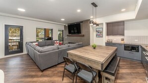 Una cocina moderna con comedor, un sofá gris y un televisor montado en la pared.