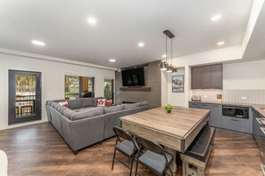 Eine moderne Küche mit Essbereich, einem grauen Sofa und einem an der Wand befestigten Fernseher.
