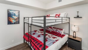Habitación con literas, un cuadro de un paisaje montañoso, una lámpara de noche y una mesita de madera.