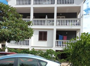 A multi-story building with balconies, a car parked in front, and greenery around. - Beach Front Apartments Jasminka (Sibenik)