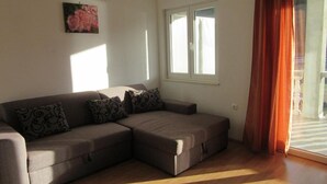 Ein Wohnzimmer mit einem Ecksofa, einem Fenster mit Vorhängen und einem Gemälde an der Wand.