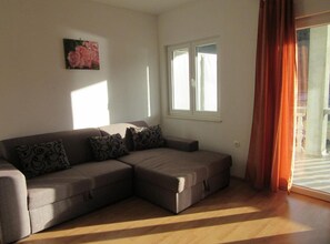 A living room with a sectional sofa, a window with curtains, and a painting on the wall. - Beach Front Apartments Jasminka (Sibenik)