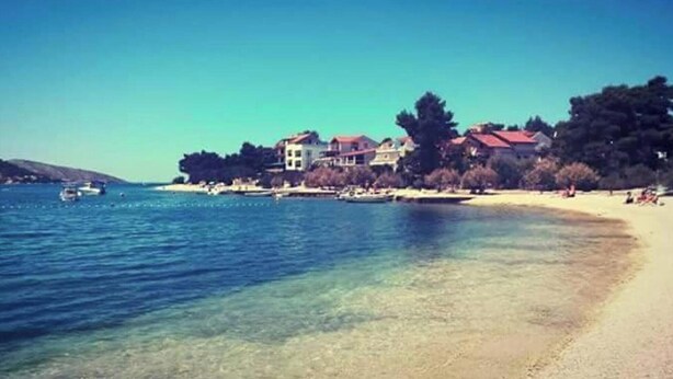 Eine Küstenlandschaft mit einem klaren Strand, ruhigem Meer und Gebäuden entlang der Uferlinie.