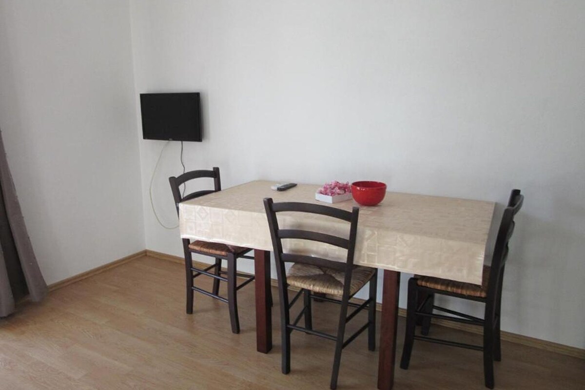 A dining area with a table, chairs, a red bowl, and a television mounted on the wall.