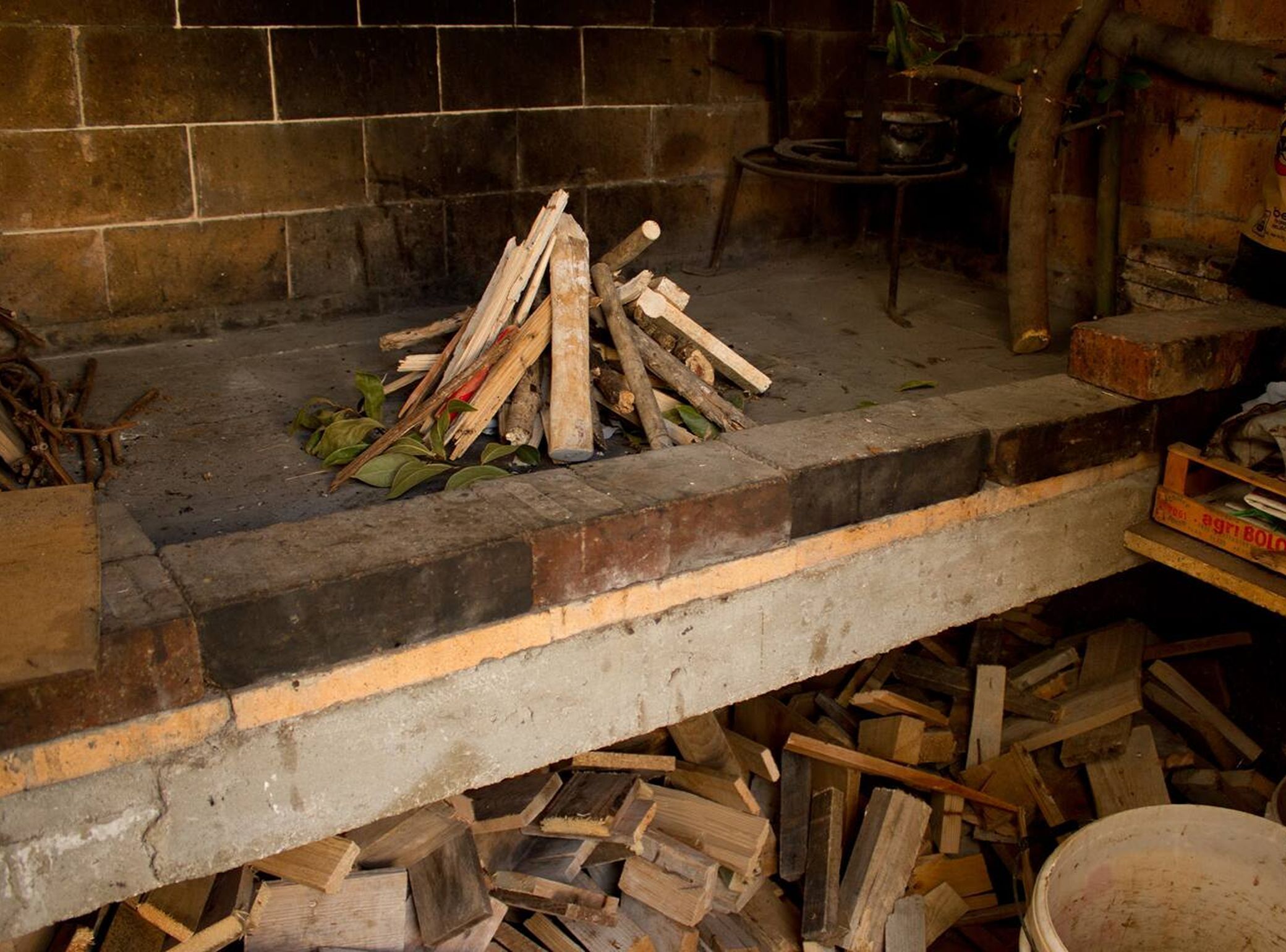 Une cheminée avec une pile de bois de chauffage et un pot en métal posé sur le foyer.