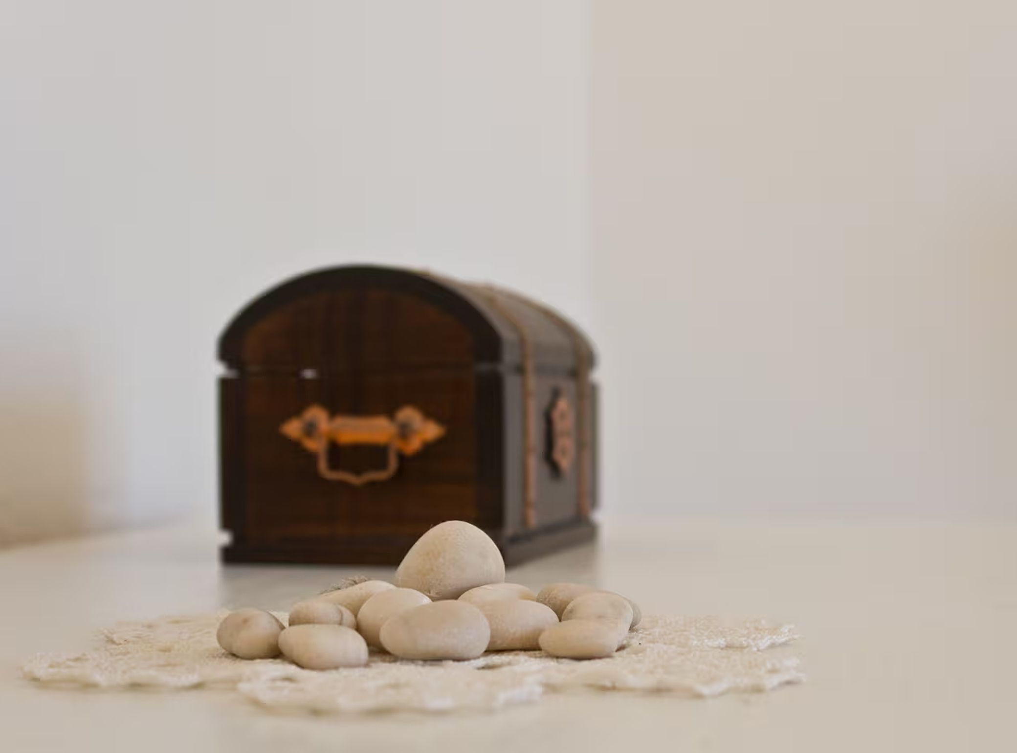 Une petite boîte en bois munie d’une poignée, posée sur une surface, avec une pile d’objets ronds devant.