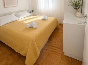 A hotel room with a bed, a nightstand, a small plant, and a white cabinet. - Apartment Karma (Okrug)