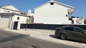 A residential street with a white house, a black fence, and a parked car. - Apartment Karma (Okrug)