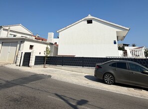 A residential street with a white house, a black fence, and a parked car. - Apartment Karma (Okrug)