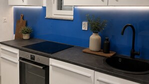 A modern kitchen with white cabinets, a black sink, a stove, and a blue backsplash. - Apartment Karma (Okrug)