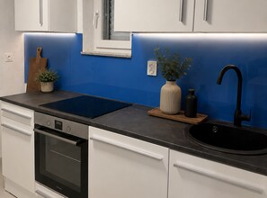 A modern kitchen with white cabinets, a black sink, a stove, and a blue backsplash. - Apartment Karma (Okrug)