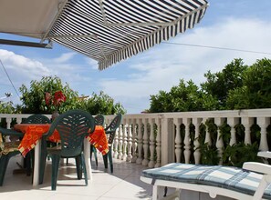 An outdoor patio area with a table and chairs, a white balustrade, and lush greenery. - Apartment Karma (Okrug)