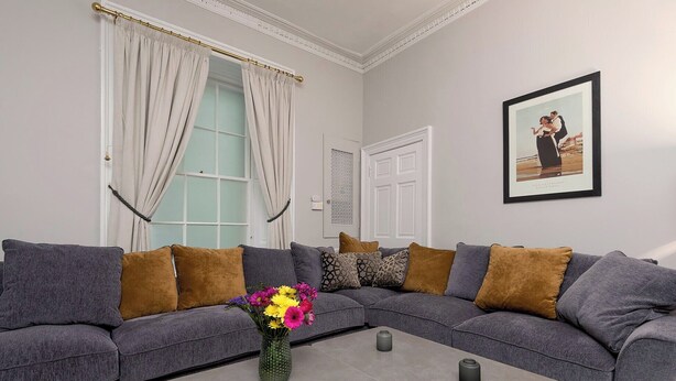 A living room with a grey sectional sofa, a coffee table, and a vase with flowers. - Two exclusive, neighbouring apartments sleeping 22 in Edinburgh’s historic centre. (Edinburgh)