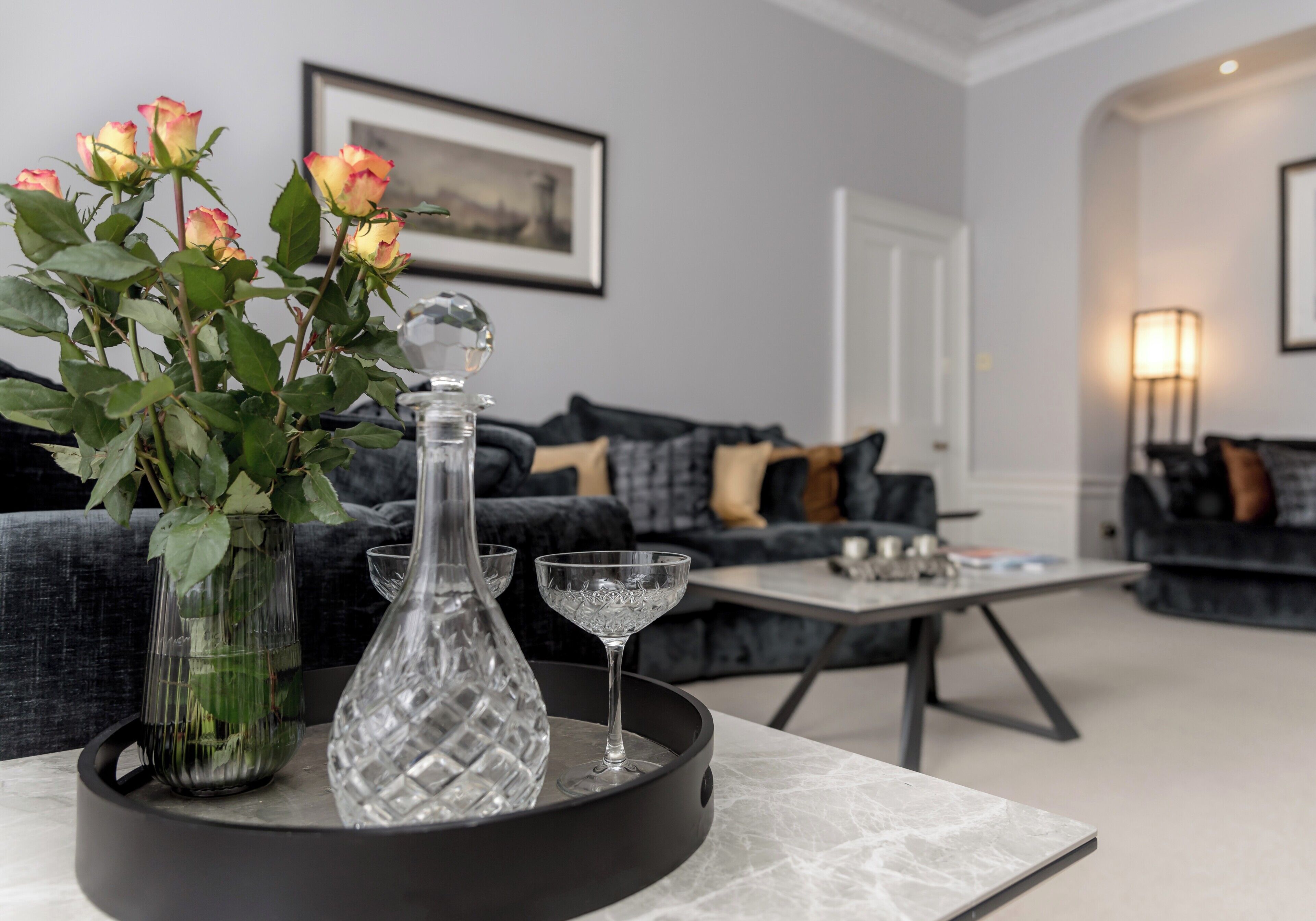 A modern living room with a sofa, a coffee table, and decorative items including a vase with flowers and a crystal decanter.