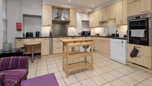 A modern kitchen with wooden cabinets, a stainless steel range hood, a dishwasher, and a small table with drawers. - Two exclusive, neighbouring apartments sleeping 22 in Edinburgh’s historic centre. (Edinburgh)