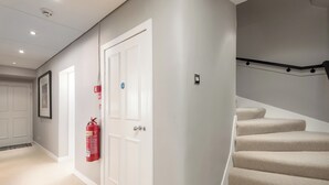 A hallway with a white door, a fire extinguisher mounted on the wall, and a staircase with beige carpet. - Two exclusive, neighbouring apartments sleeping 22 in Edinburgh’s historic centre. (Edinburgh)