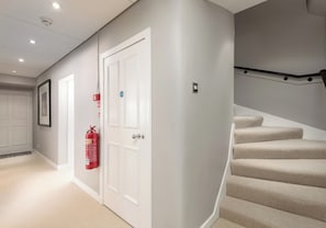 Ein Flur mit einer weißen Tür, einem an der Wand befestigten Feuerlöscher und einer Treppe mit beigem Teppich.