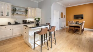 A modern kitchen with white cabinetry, a central island, and bar stools. - Two exclusive, neighbouring apartments sleeping 22 in Edinburgh’s historic centre. (Edinburgh)