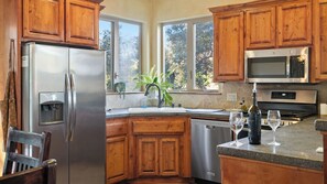 A kitchen with wooden cabinets, stainless steel appliances, a dishwasher, and a window with a view of trees. - Vita Amorosa by Avantstay Gated Cottage + Oak & Vineyard Views Near Paso Robles (Atascadero)