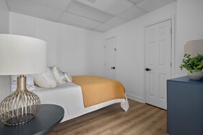 Ein Schlafzimmer mit einem Bett, einem Nachttisch mit Lampe, einer Zimmerpflanze und einer Tür.
