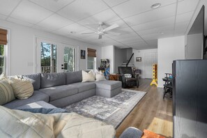 Ein geräumiges Wohnzimmer mit einem Ecksofa, Deckenventilator und einem großen Fenster.