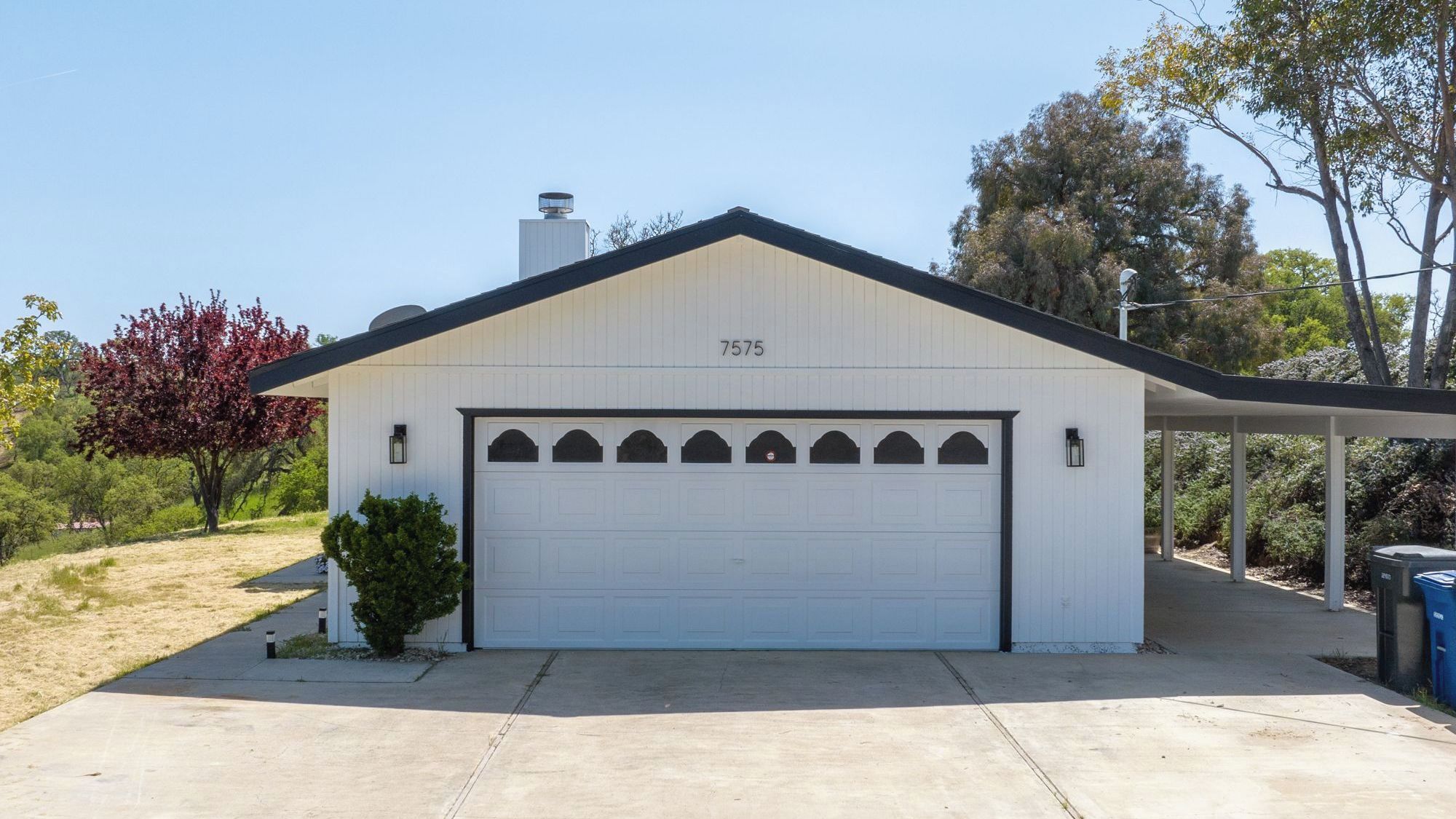 A single-story building with a white garage door, a number '7575' on the wall, and a small attached structure with a roof.