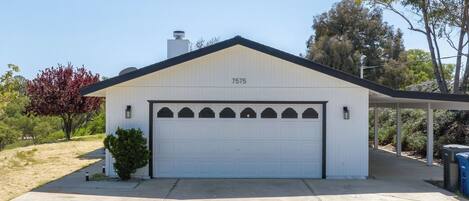 A single-story building with a white garage door, a number '7575' on the wall, and a small attached structure with a roof.
