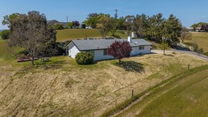A single-story house with a sloped roof, surrounded by a grassy area and trees. - Whispering Wine by Avantstay Country Acreage + Fire Pit + Deck Central Coast Wine Country (Paso Robles)