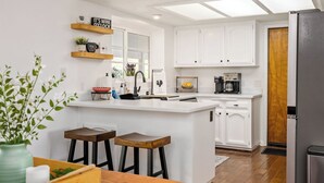 A modern kitchen with white cabinetry, a central island with stools, a coffee machine, and a refrigerator. - Whispering Wine by Avantstay Country Acreage + Fire Pit + Deck Central Coast Wine Country (Paso Robles)
