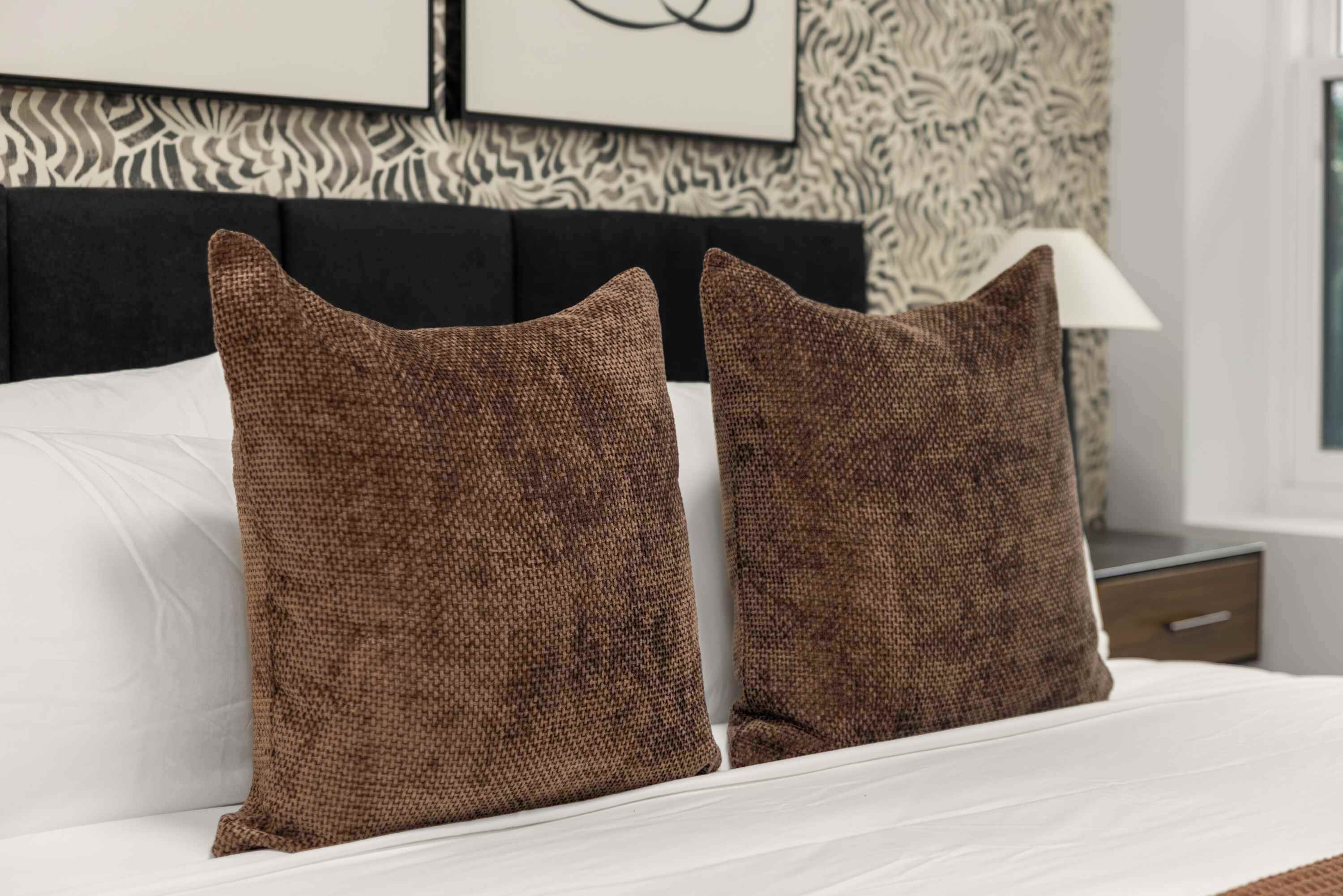 Una cama con dos almohadas cuadradas y un colchón blanco.