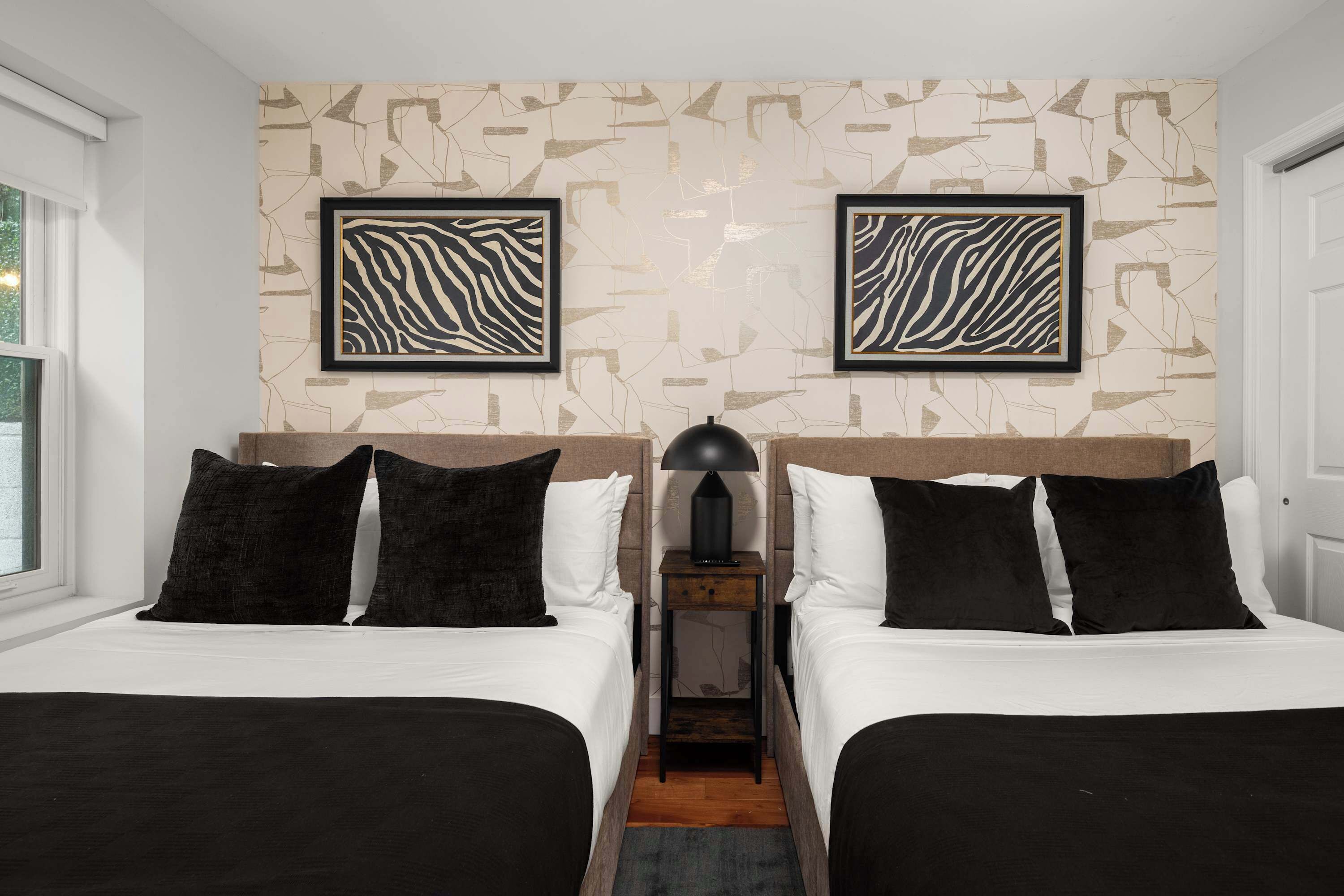 Habitación de hotel con dos camas, una mesita de noche con lámpara y arte abstracto en la pared.