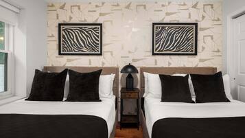 Habitación de hotel con dos camas, una mesita de noche con lámpara y arte abstracto en la pared.