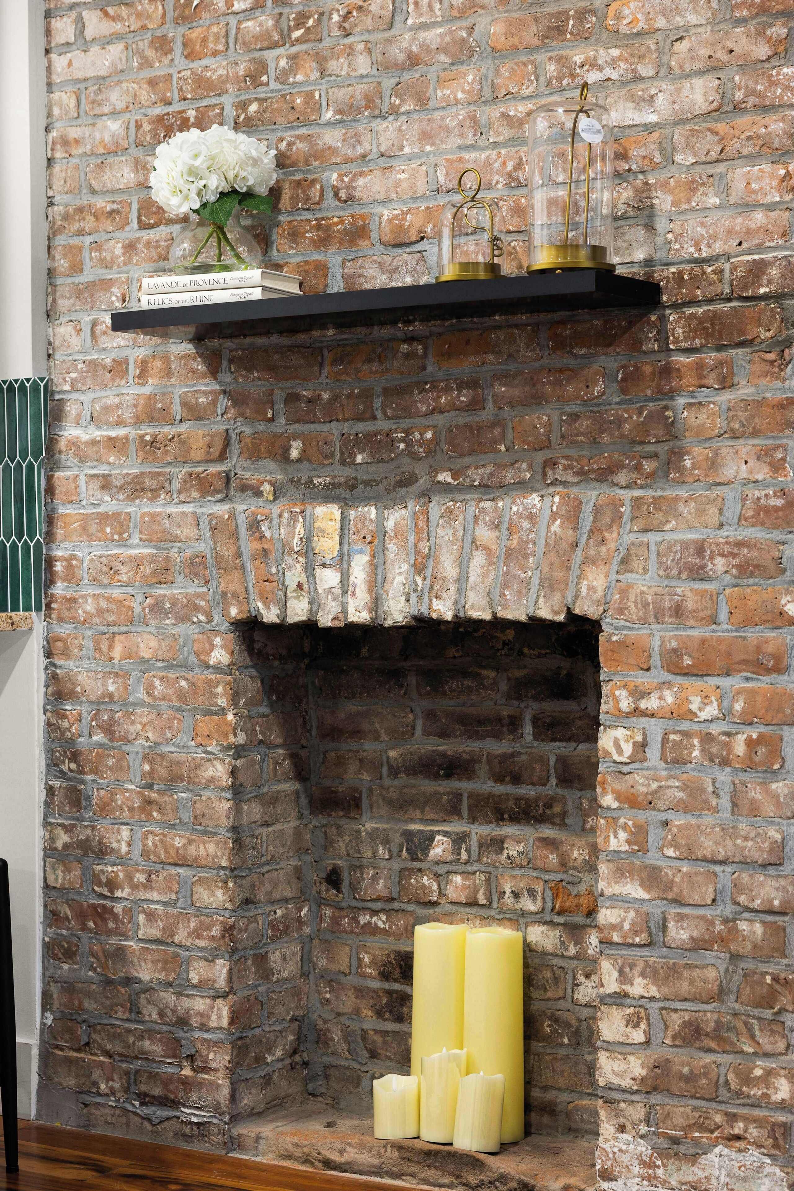 A brick fireplace with a shelf above it holding books and a vase with flowers.