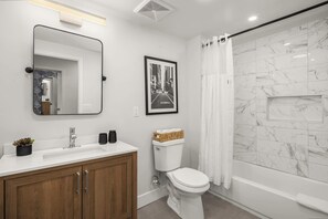 Uma casa de banho moderna com um lavatório branco, uma sanita e um chuveiro com parede de mármore, e um quadro emoldurado na parede.