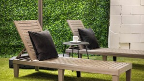 A lounge area with two wooden lounge chairs, each with a cushion, and a small round table with a cup and saucer.