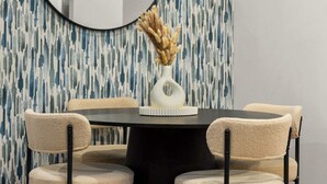 A dining area with a round table, four chairs, a vase with dried flowers, and a large mirror on the wall.