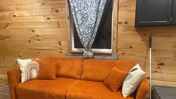 Interior em madeira com sofá, cortinas estampadas e abajur.