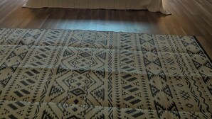 Un dormitorio con techo inclinado, un ventanal grande, una cama con almohadas, dos lámparas de noche y una alfombra estampada.