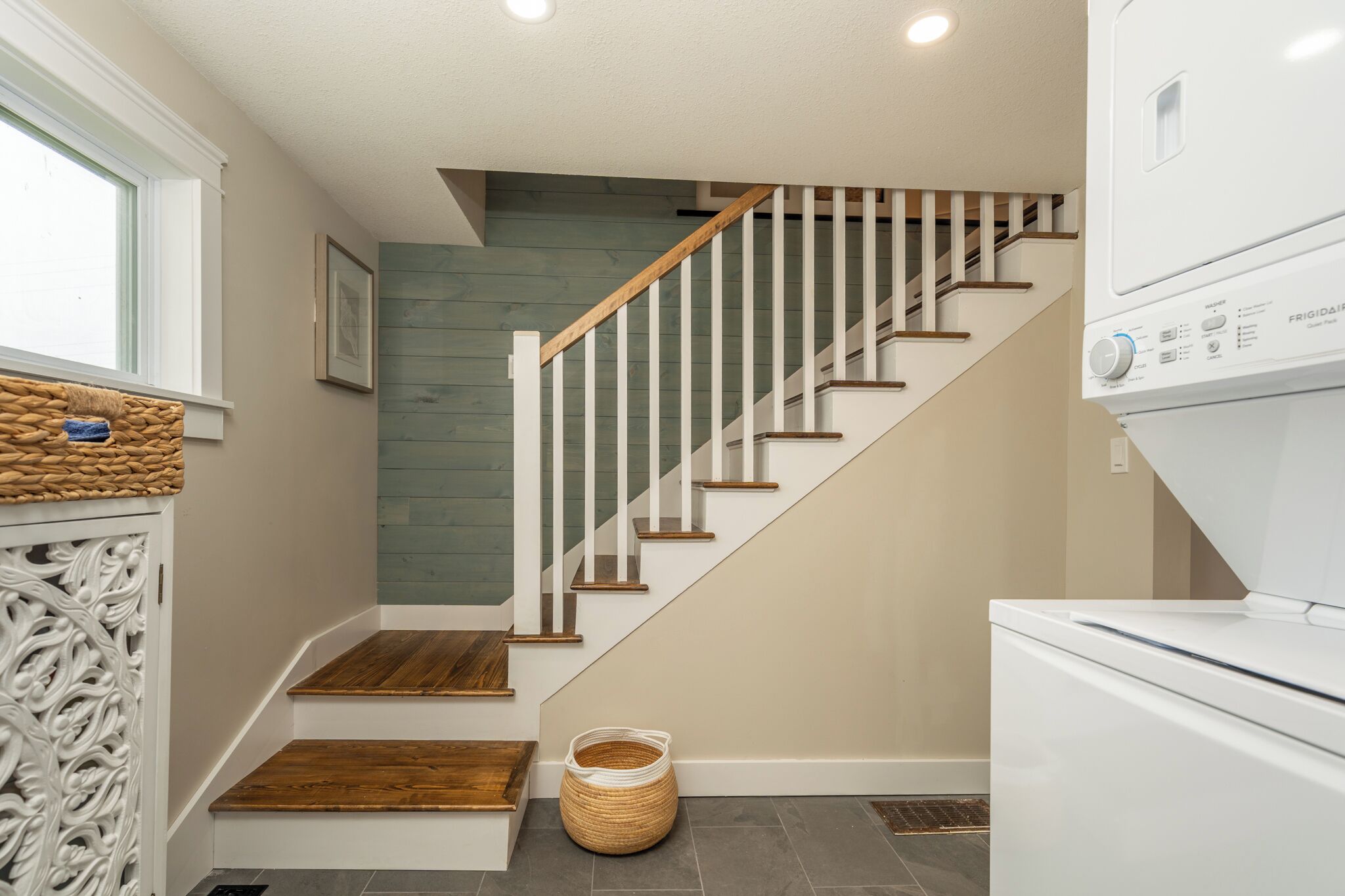 A staircase with wooden steps and white railings, leading to a landing with a white appliance and a woven basket.