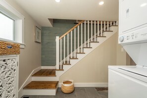 A staircase with wooden steps and white railings, leading to a landing with a white appliance and a woven basket.