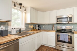 Una cocina moderna con armarios blancos, una estufa de acero inoxidable, un microondas y una cafetera.